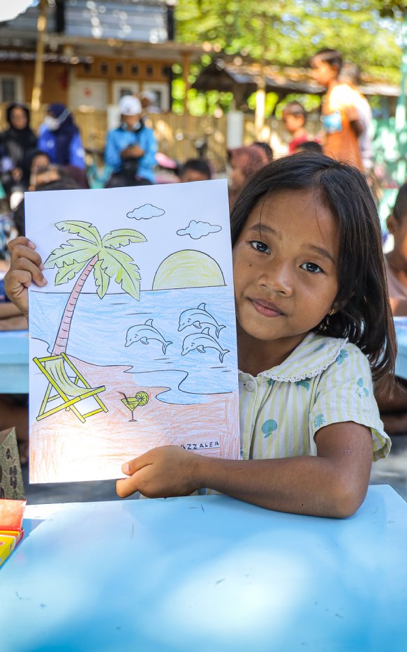Seorang anak dengan bangga menunjukkan gambar pantai dan lumba-lumba hasil karyanya—simbol sederhana dari imajinasi, harapan, dan pentingnya literasi sejak dini bagi setiap anak di NTB. Foto: © Tim Komunikasi INOVASI 2025